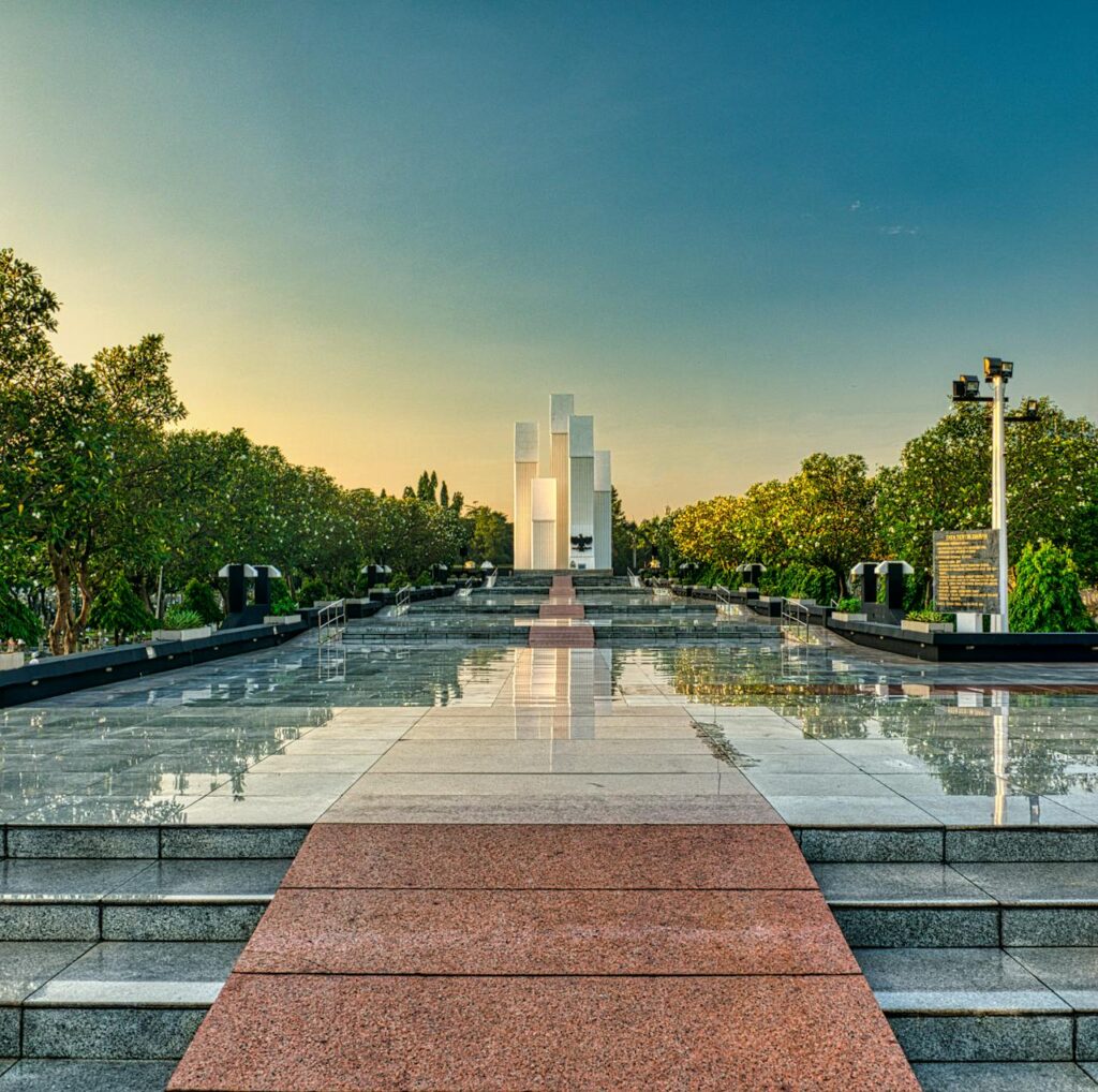 Granite pathway with steps among lush green trees leading to modern tall building in national main heroes cemetery in Kalibata