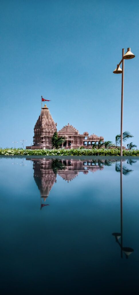 A stunning view of a Hindu temple reflecting in calm water under a bright blue sky.