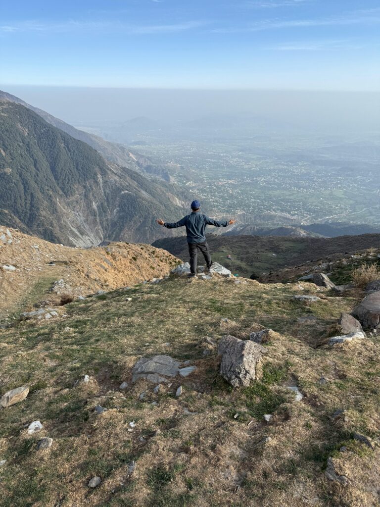 A person stands on a hill overlooking the breathtaking Dharamshala Valley landscape.