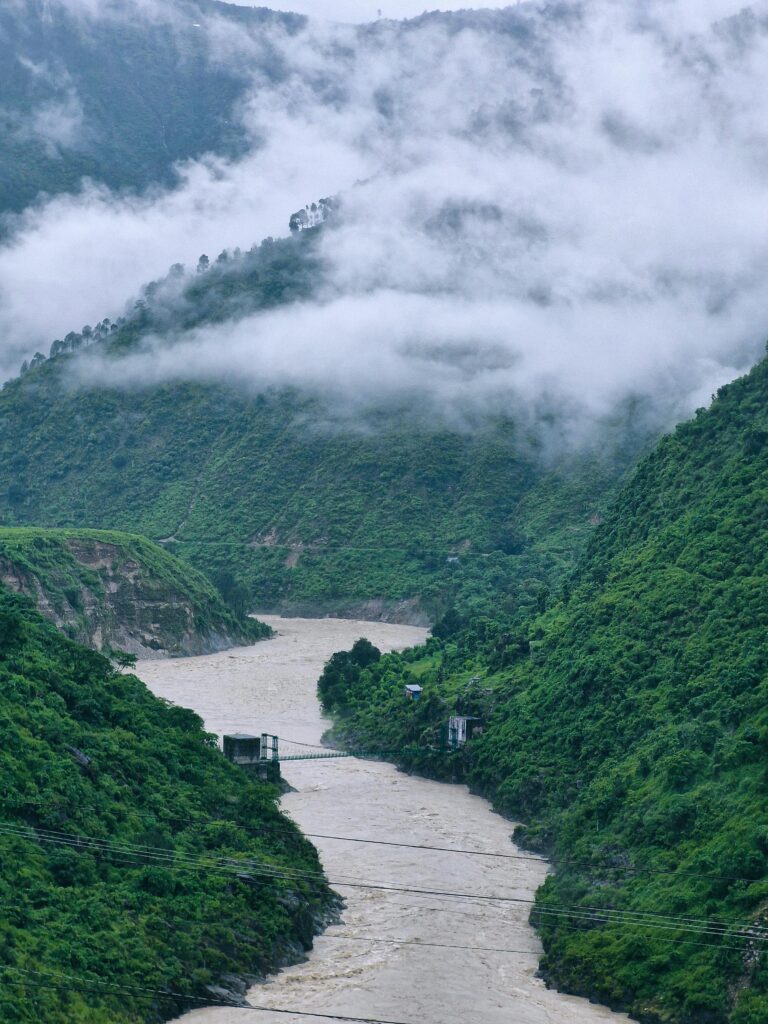 Serene mist over lush green Himalayan valley with river flowing through, captured in Uttarakhand, India.