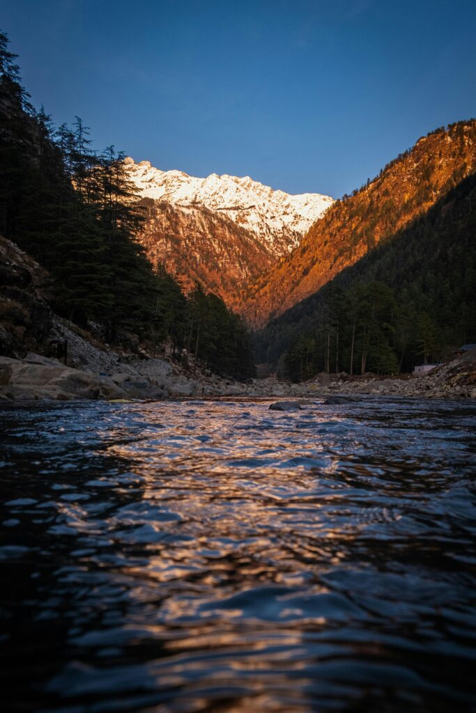 Beautiful scene of a river reflecting snow-capped Himalayan mountains during sunrise in Kasol, India.
