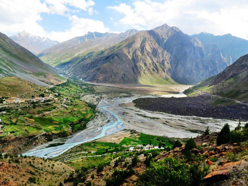 Serene river valley surrounded by towering mountains under a clear blue sky, perfect for nature enthusiasts.